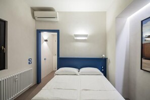 Ein Hotelzimmer mit Bett, Klimaanlage, Leuchte und einer Tür zu einem weiteren Raum.