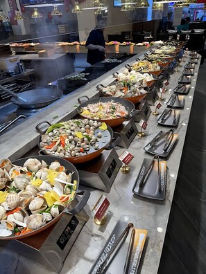 A buffet with various seafood dishes, including clams and mushrooms, and a person in the background. - Vinhomes Skylake Apartment - Layia Homes (Hanoi)