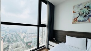 A hotel room with a large window, a bed, a nightstand, and a painting. - Vinhomes Skylake Apartment - Layia Homes (Hanoi)
