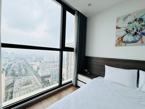 A hotel room with a large window, a bed, a nightstand, and a painting. - Vinhomes Skylake Apartment - Layia Homes (Hanoi)