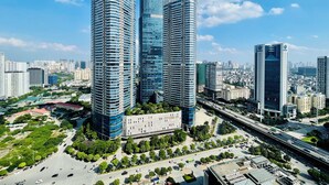 A cityscape with modern high-rise buildings, a central plaza with greenery, and a busy road. - Vinhomes Skylake Apartment - Layia Homes (Hanoi)
