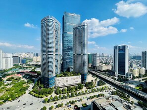 A cityscape with modern high-rise buildings, a central plaza with greenery, and a busy road. - Vinhomes Skylake Apartment - Layia Homes (Hanoi)