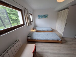 A bedroom with two beds, a radiator, a window with curtains, a bedside lamp, and a painting on the wall. - Quiet house near the ocean: 8 adults + 2 children (Baden)