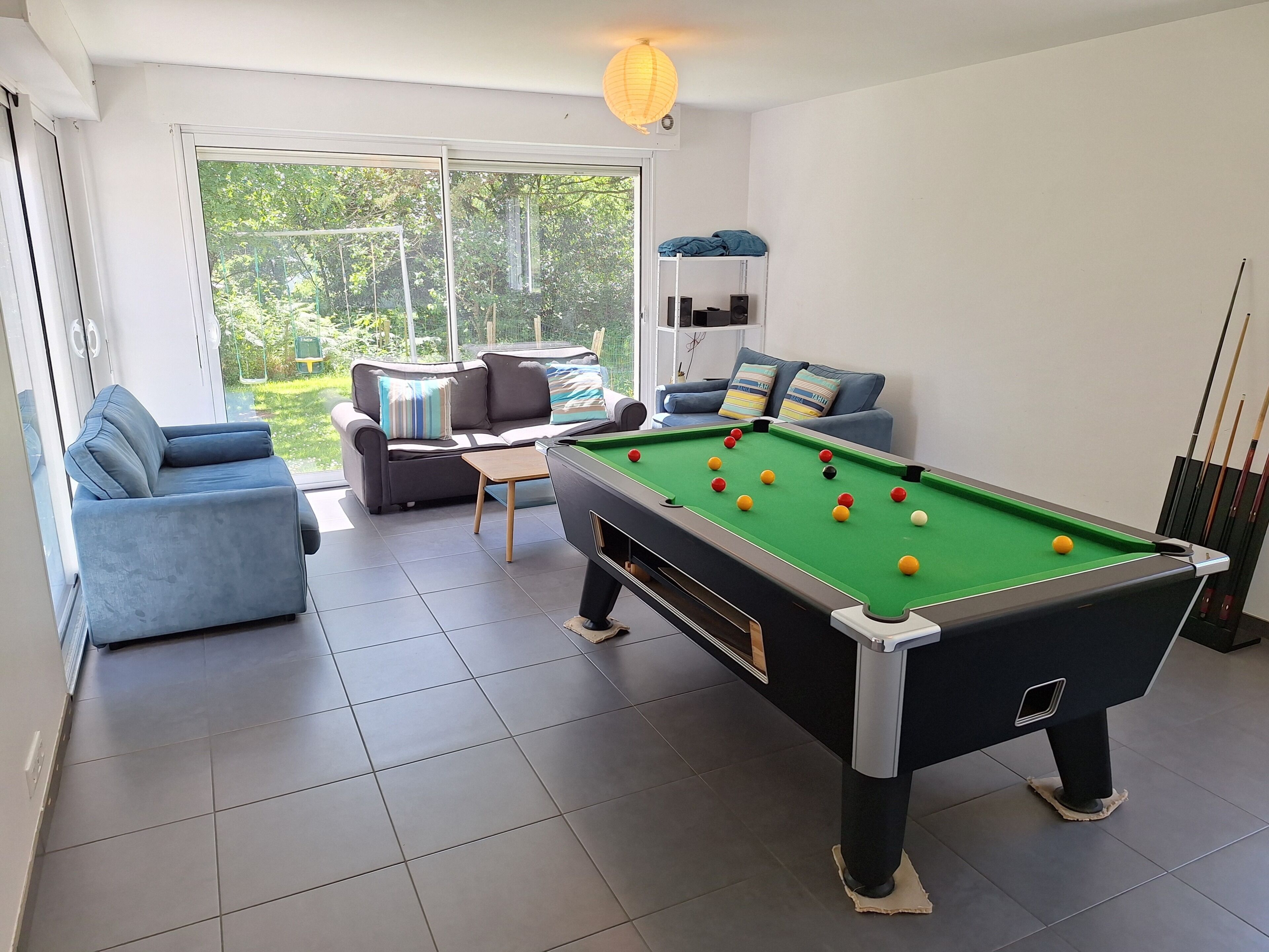 A pool table with balls, a sofa, a coffee table, and a window with a view of greenery.