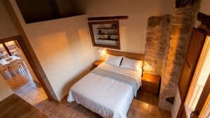 Un dormitorio con cama, mesitas de noche, pared de piedra y puerta de madera.