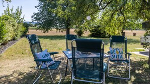 Een terras met drie stoelen en een tafel, omringd door bomen en uitzicht op het landschap.