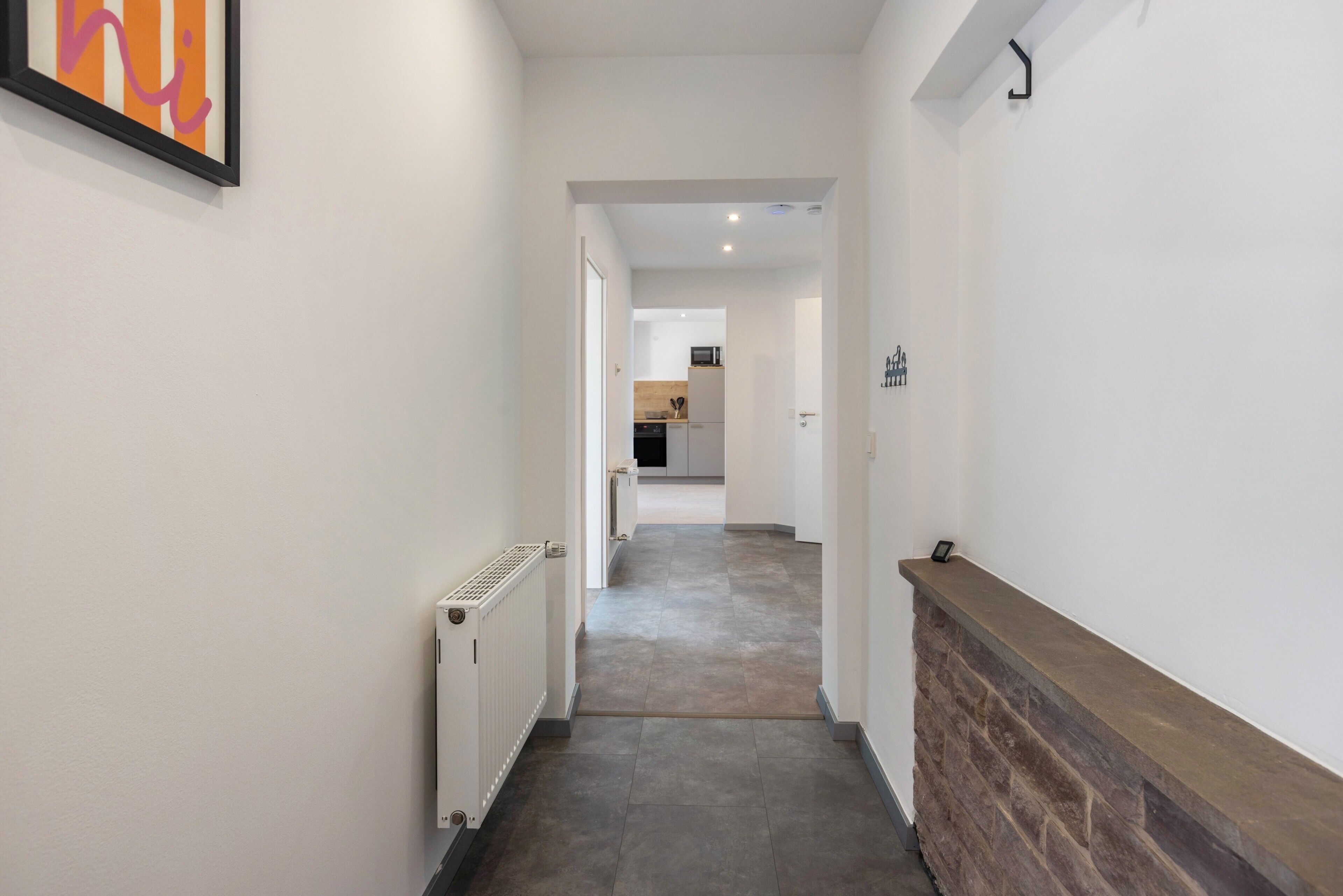 A hallway with a radiator, a fireplace, and a kitchen visible in the distance.