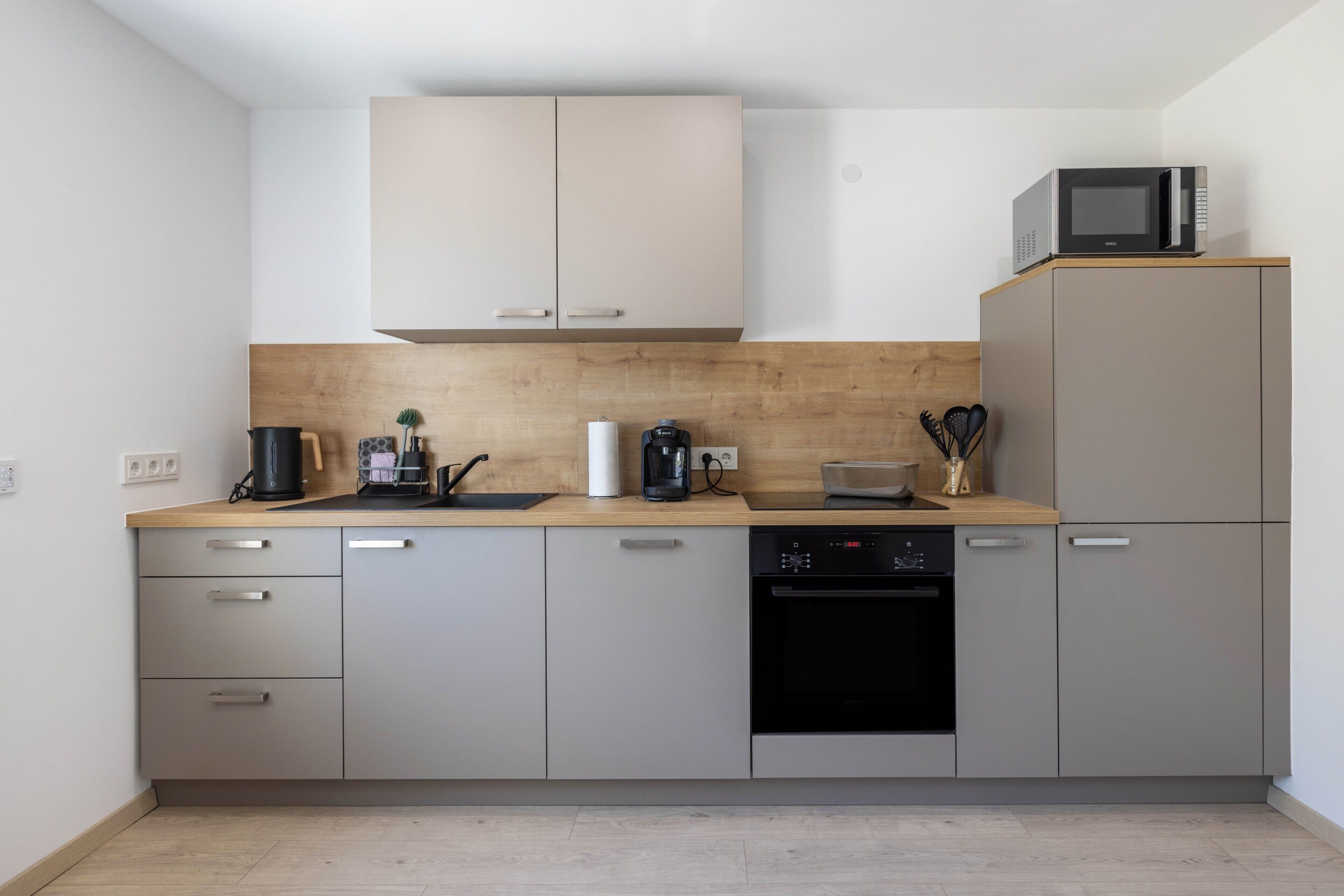 Eine moderne Küche mit grauen Schränken, einer Holz Arbeitsplatte, einer Mikrowelle, einer Kaffeemaschine und einem Geschirrspüler.