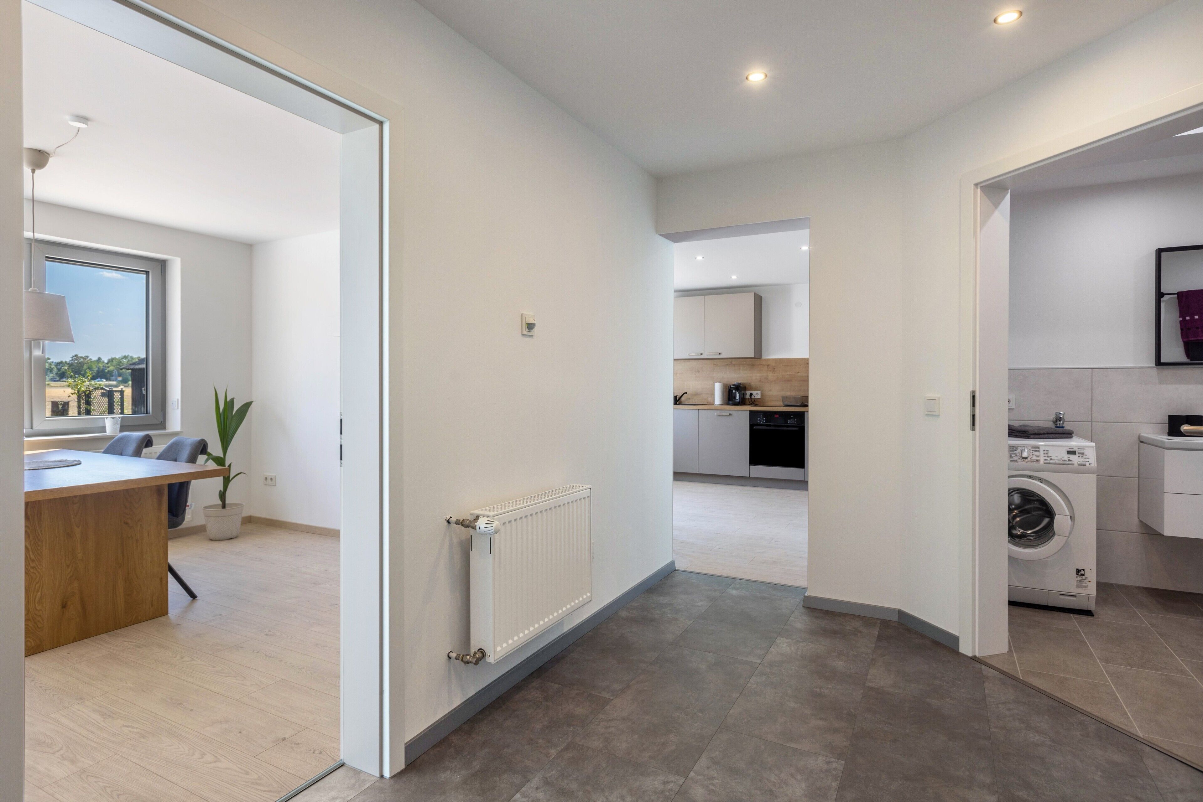 A modern kitchen with a built-in oven, a washing machine, and a dining area with a table and chairs.