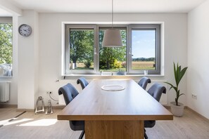 Comedor moderno con una mesa grande, sillas, una ventana que ofrece vistas a zonas verdes, y una lámpara colgante.