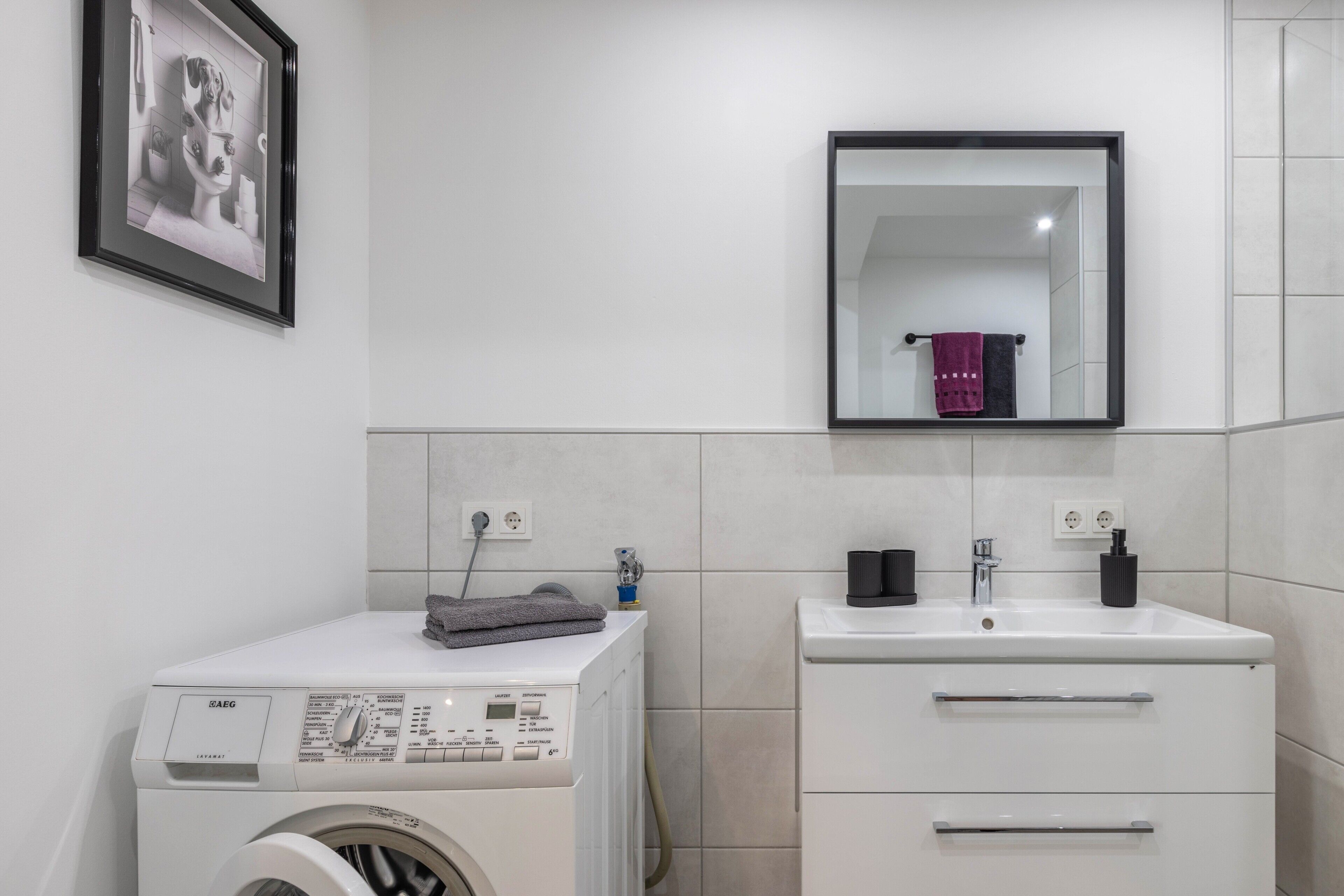 Ein modernes Badezimmer mit Waschmaschine, Waschbecken und Spiegel.