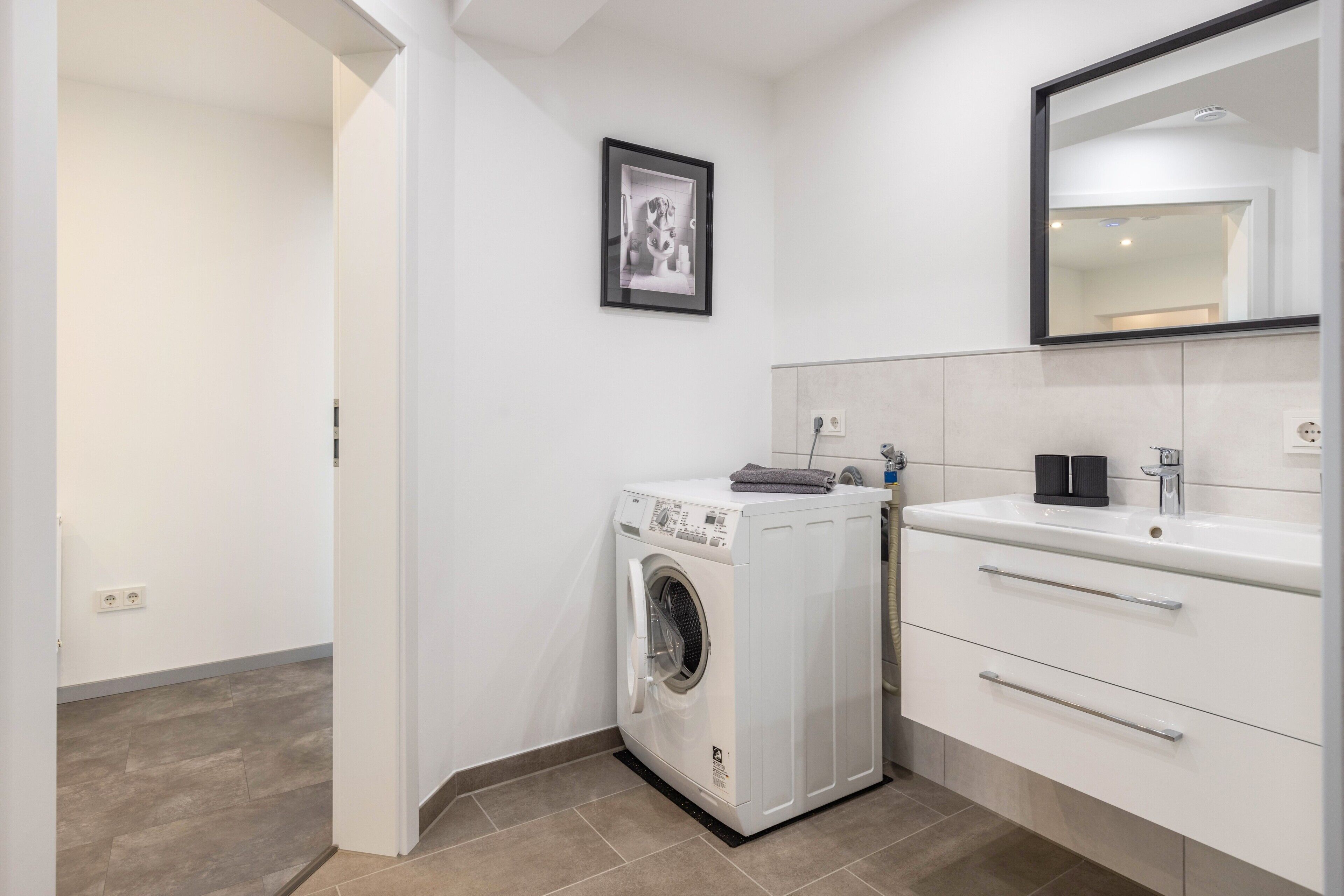 A compact, modern bathroom with a washing machine, a sink, and a mirror.