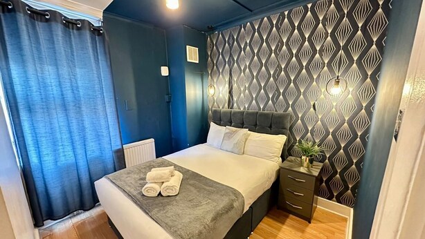 Un dormitorio con cama, mesitas de noche, radiador y pared con estampado.