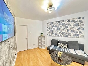 A living room with a sofa, a coffee table, a TV mounted on the wall, and a ceiling light fixture. - South London, Perfectly Placed (London)
