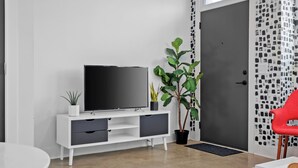 A modern living room with a flat-screen TV on a white console, a potted plant, and a red chair. - NEW! 2 NashHomes! The Perfect Couple (Nashville)