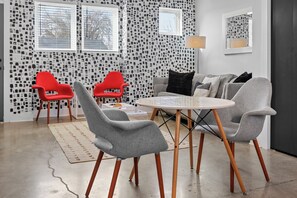 Ein modernes Wohnzimmer mit einem runden Tisch und grauen Stühlen, einem roten Sessel und einem grauen Sofa mit strukturierten Tapeten und einem Spiegel.