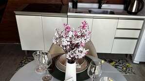 Ein Esstisch ist gedeckt mit Tellern, Gläsern und Besteck, in der Mitte steht eine Blumenvase.