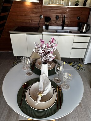 Ein Esstisch ist gedeckt mit Tellern, Gläsern und Besteck, in der Mitte steht eine Blumenvase.