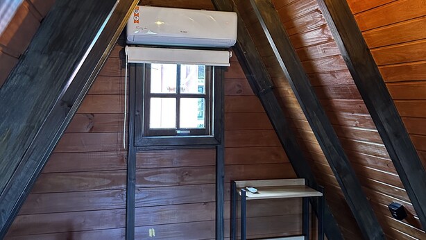 Ein Dachzimmer mit schrägen Wänden, einem Fenster mit Blick und einer eingebauten Klimaanlage sowie einem kleinen Tisch.