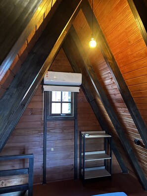 An attic room with a sloped ceiling, a window with a view, a built-in air conditioning unit, and a small table. - Cabana Riviera Ferrugem (Garopaba)