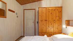 Quarto com uma cama, um guarda-roupa de madeira, uma porta e um espelho na parede.