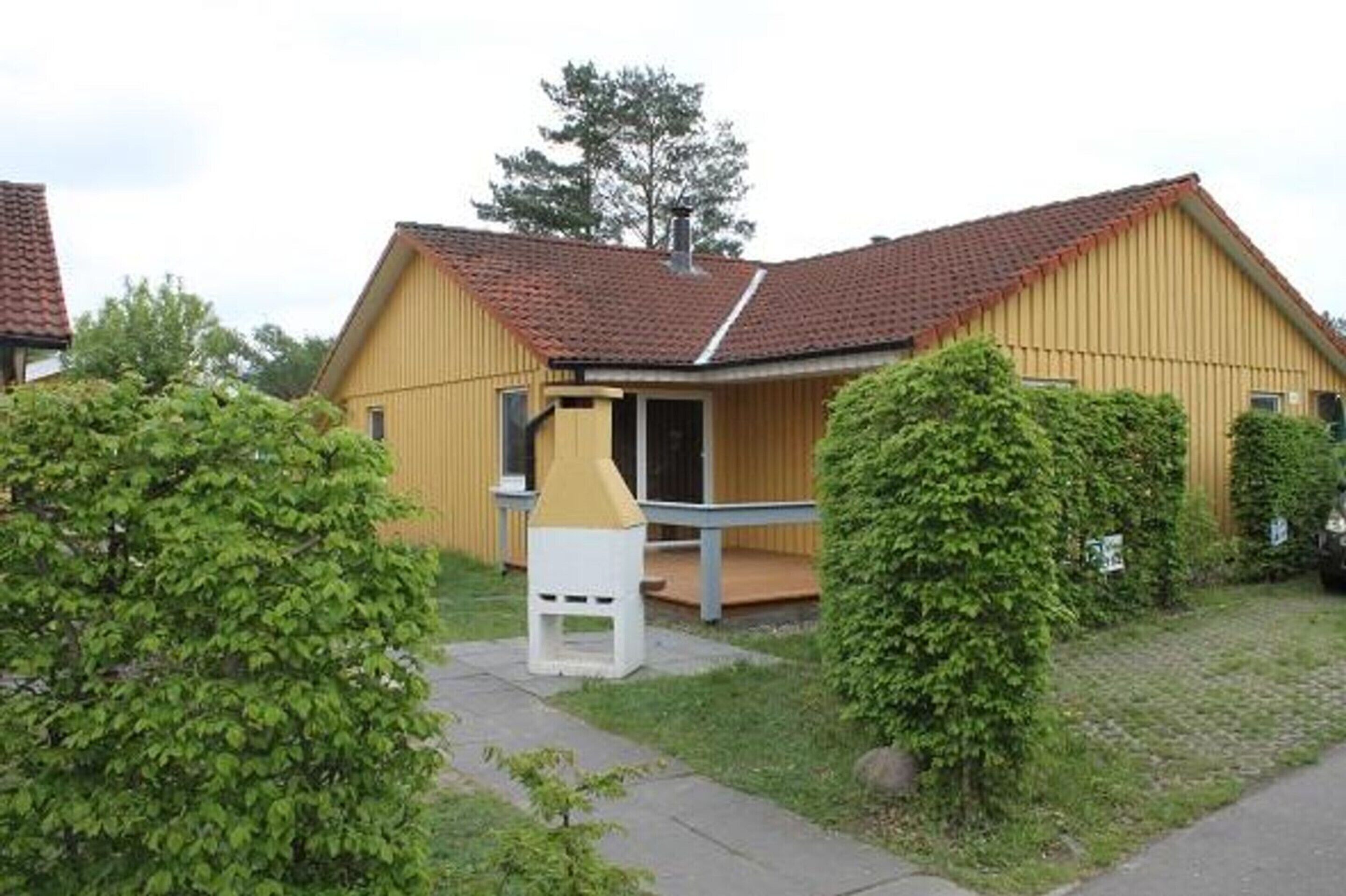 A yellow building with a red-tiled roof, a small porch, and a white structure in front.