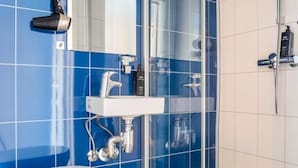 A bathroom with a white sink, a mirror, a handheld showerhead, and a hairdryer mounted on the wall. - Lofoten Bed & Breakfast (Moskenes)