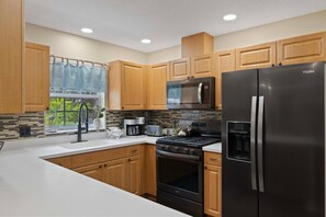 Una cocina moderna con armarios de madera, un refrigerador de acero inoxidable, un microondas, una estufa y una cafetera.