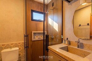 Ein Badezimmer mit Holzwaschtisch, Duschkabine aus Glas und kleinem Fenster.