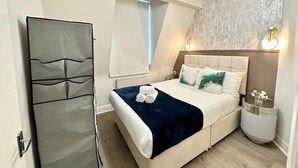 A bedroom with a bed, a bedside table, a wall-mounted light, and a window. - Apartment at Albert House, Kennington (London)
