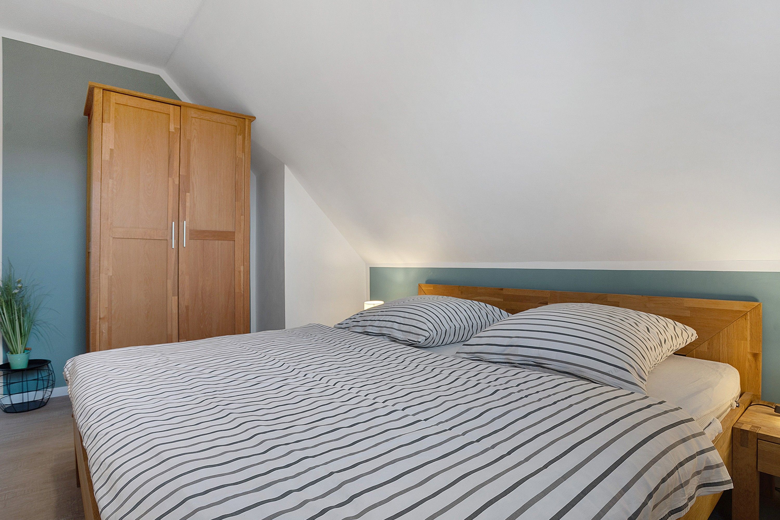Ein Schlafzimmer mit einem Bett, einem Nachttisch, einer Lampe, einem Holzschrank und einem Topfpflanze.