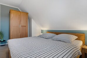 Ein Schlafzimmer mit einem Bett, einem Nachttisch, einer Lampe, einem Holzschrank und einem Topfpflanze.
