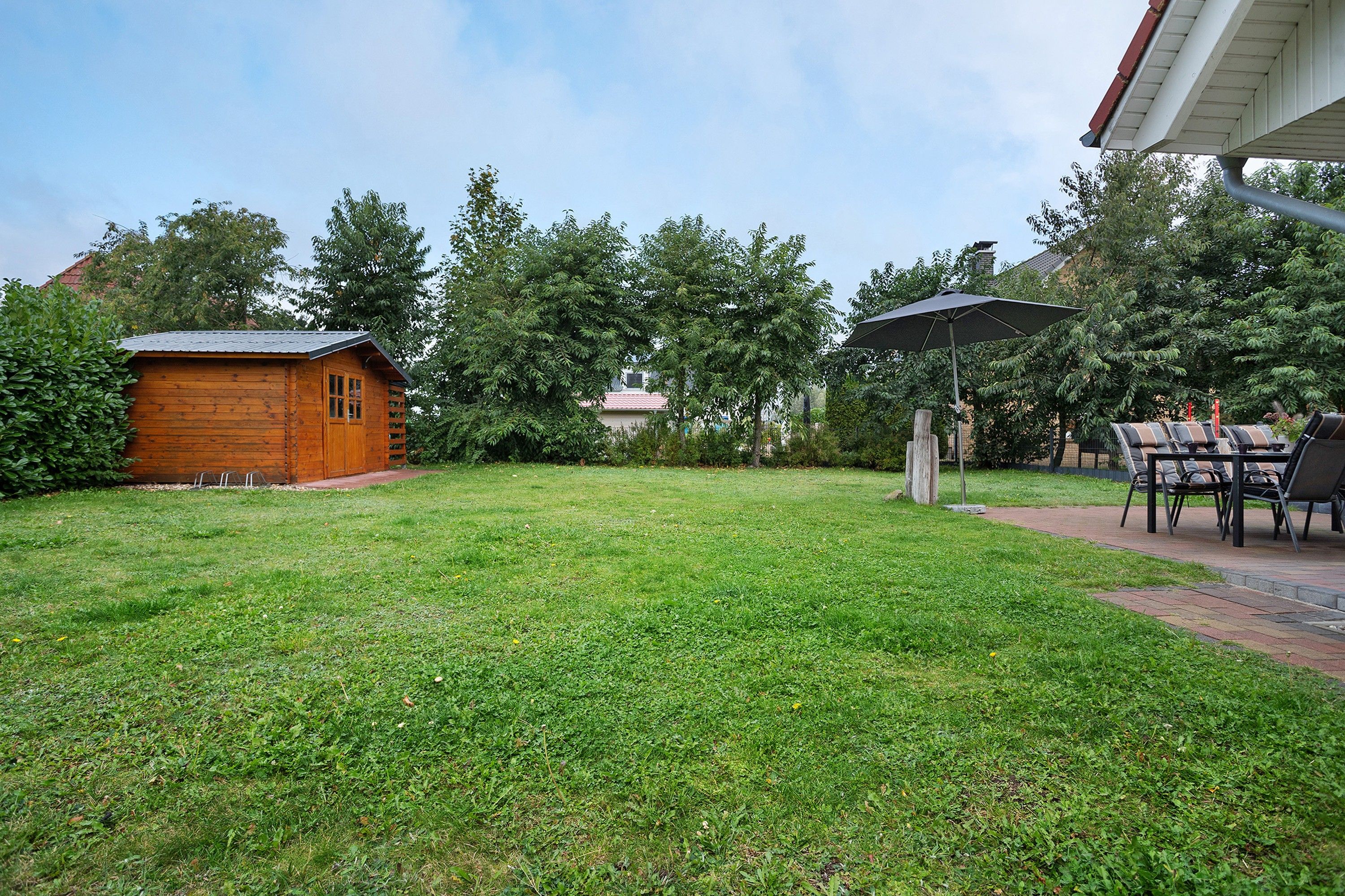 Ein Garten mit einem Holler Schuppen, einem Patio-Tisch mit Stühlen und einer Rasenfläche.