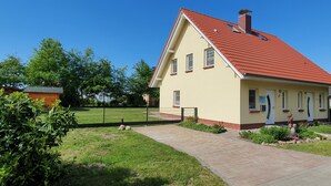 Una casa de dos pisos con techo rojo, entrada pavimentada y patio cercado.