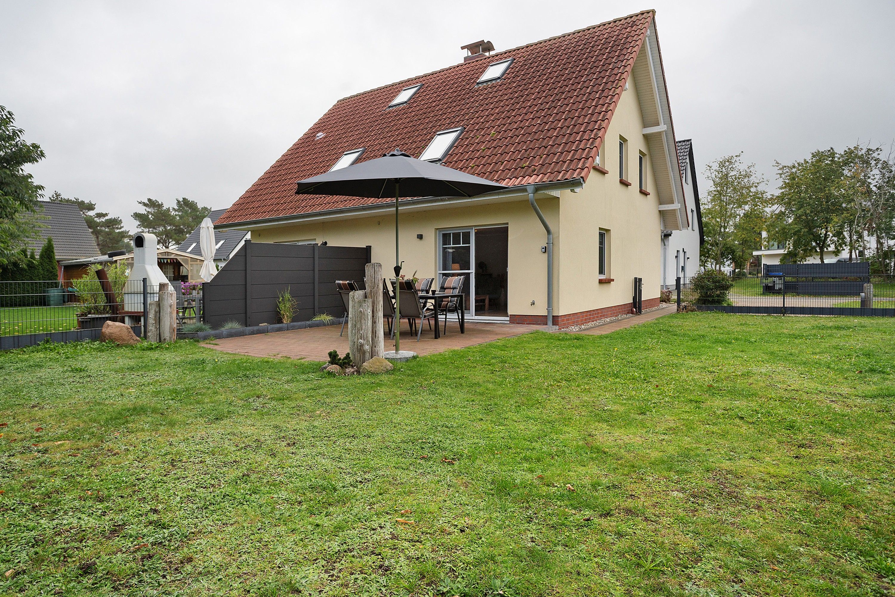 A two-story house with a red-tiled roof, a covered patio area with outdoor furniture, and a fenced yard.