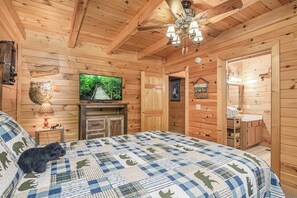 A wooden cabin bedroom with a bed, a television, a fireplace, and a small table with a lamp. - Smoky Mtn Lake Escape | Hot Tub | Sleeps 7 (Sevierville)