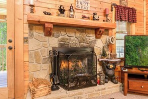 A stone fireplace with a glass screen, surrounded by wooden decor and a bear statue. - Smoky Mtn Lake Escape | Hot Tub | Sleeps 7 (Sevierville)