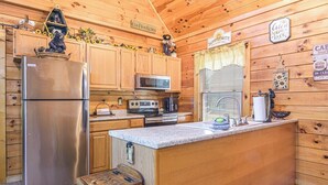 Cozinha de uma cabana rústica, com geladeira, micro-ondas, fogão e armários de madeira.