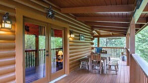 Uma cabana de madeira com varanda, uma mesa e cadeiras, e uma placa indicando uma pousada.