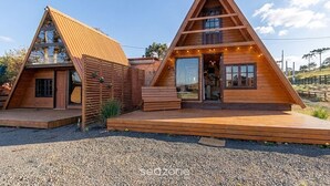 Two wooden triangular cabins with a porch and a small outdoor seating area. - House w/ Jacuzzi & Mountain View Rcn0000 (Urubici)