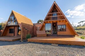 Zwei hölzerne, dreieckige Blockhütten mit Veranda und kleiner Sitzgelegenheit im Freien.