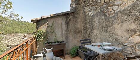 Un patio al aire libre con una mesa lista para comer, rodeado de muros de piedra y una barandilla de metal.