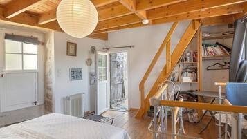 Een slaapkamer met een bed, een radiator, een houten plafond, een raam met jaloezieën en een boekenkast.