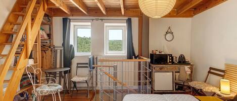 A cozy room with a bed, a desk, a chair, a ladder, and a view of the outdoors through a window.
