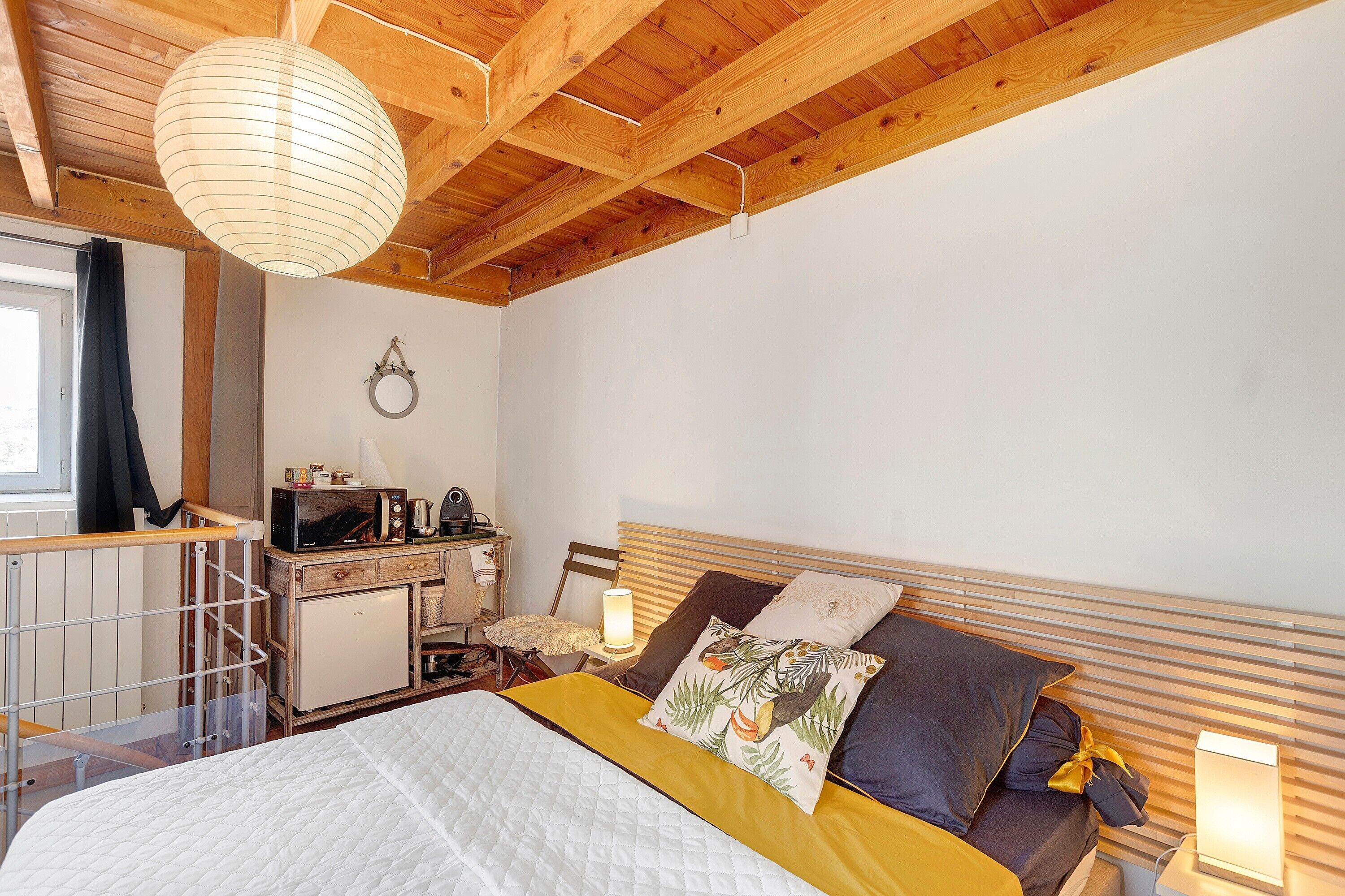 Une chambre à coucher avec un lit, des lampes de chevet, une petite table avec un micro-ondes et une fenêtre avec des rideaux.