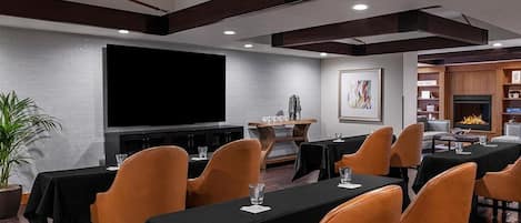 Een vergaderzaal met tafels en stoelen, een groot scherm en een open haard.
