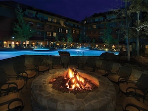 A nighttime outdoor seating area with a fire pit, lounge chairs, and a pool in the background. - Studio Villa Lake Tahoe Grand Residence Resort (South Lake Tahoe)
