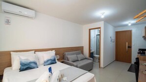 A hotel room with a bed, a sofa, a small table, a kitchenette, and a bathroom. - Studio in Condo. w/ Pool & Coworking Azz0305 (Cabedelo)