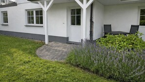 Un edificio bianco con un portico coperto, un piccolo giardino con lavanda e un vialetto lastricato.