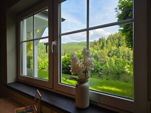 A room with a large window, a vase with flowers, and a window sill with a chair and a tray of pens.